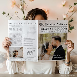 Könnte beinhalten: Eine Hochzeitsanzeige im Zeitungsstil mit der Überschrift "The Newlywed Times". Die Titelseite zeigt ein Foto eines sich küssenden Paares, ein Suchworträtsel und ein Kreuzworträtsel. Die Anzeige wird von einer Person gehalten.