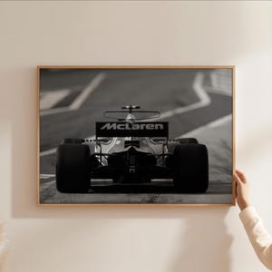Puede incluir: Fotograf&iacute;a en blanco y negro de un coche de carreras de F&oacute;rmula 1 McLaren en una pista. El coche est&aacute; de frente a la c&aacute;mara y el logotipo de McLaren es visible en el aler&oacute;n trasero.