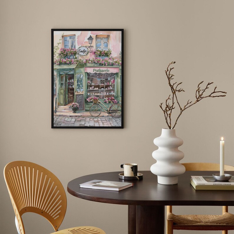 May include: A watercolour painting of a French bakery with a bicycle parked in front. The bakery is called "Emily's Patisserie" and has a green awning. The building is painted in soft pink and white colours.