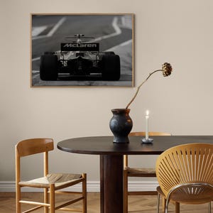 Puede incluir: Una fotograf&iacute;a en blanco y negro de un coche de carreras de F&oacute;rmula 1 McLaren en una pista. El coche est&aacute; de cara a la c&aacute;mara y el logotipo de McLaren es visible en la parte trasera del coche.