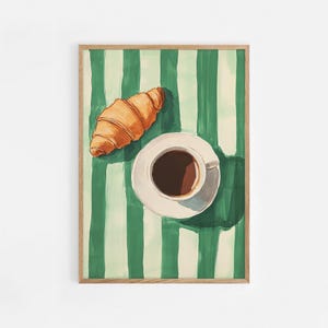 May include: A top-down view of a cup of coffee and a croissant on a green and white striped tablecloth. The coffee is in a white cup and saucer, and the croissant is golden brown.