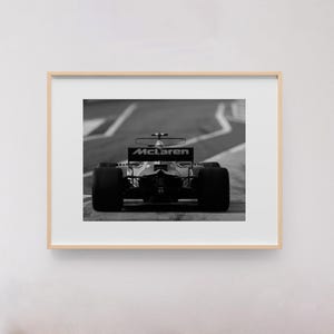 Puede incluir: Una fotograf&iacute;a en blanco y negro de un coche de carreras de F&oacute;rmula 1 McLaren en una pista. El coche est&aacute; de cara a la c&aacute;mara y el logotipo de McLaren es visible en el aler&oacute;n trasero.
