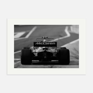 Puede incluir: Una fotograf&iacute;a en blanco y negro de un coche de carreras de F&oacute;rmula 1 McLaren conduciendo en una pista. El coche est&aacute; de espaldas a la c&aacute;mara y el logotipo de McLaren es visible en la parte trasera del coche.