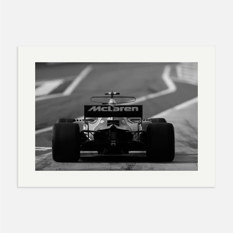 Puede incluir: Una fotograf&iacute;a en blanco y negro de un coche de carreras de F&oacute;rmula 1 McLaren conduciendo en una pista. El coche est&aacute; de espaldas a la c&aacute;mara y el logotipo de McLaren es visible en la parte trasera del coche.
