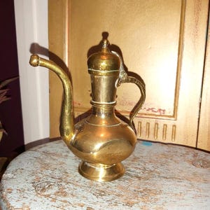 May include: A small, gold-coloured brass teapot with a curved spout and a handle. The teapot has a decorative lid and a round body.
