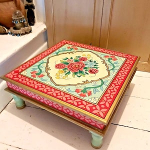 May include: A square wooden table with hand-painted floral designs in shades of pink, green, and yellow. The table has four legs painted a light green colour.