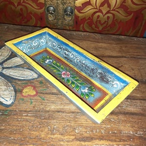 May include: A rectangular wooden tray featuring a bright yellow border and a blue interior base. The centre of the tray is decorated with a hand-painted floral vine motif in green, pink, and white, while the side walls display a white scroll pattern.