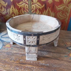 May include: A round wooden bowl with a light natural finish, featuring carved star patterns on the exterior. The bowl is reinforced with dark metal bands secured by small rivets and stands on four short, sturdy wooden legs.