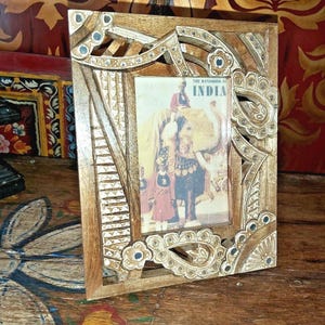 May include: A rectangular wooden picture frame featuring intricate hand-carved patterns and small inlaid mirrors. The frame holds a vintage-style print depicting an elephant and figures with the text THE HANDBOOK OF INDIA printed at the top.