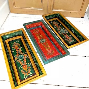 May include: Three rectangular wooden trays with hand-painted floral designs. The trays are painted in shades of green, red, orange, and gold.