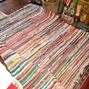 May include: A colourful, striped, woven rug with fringed edges. The rug is made from recycled materials and has a rustic, bohemian style.