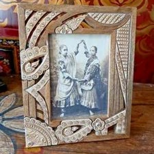 May include: A rectangular wooden picture frame featuring intricate hand-carved paisley and floral patterns. The frame holds a sepia-toned photograph of two individuals standing side-by-side, holding hands and wearing traditional garments.