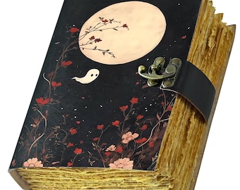 May include: A vintage-style journal with a black cover featuring a full moon, flowers, and a ghost illustration. The journal has a leather strap closure and aged paper pages. The cover art is in shades of red, white, and black.
