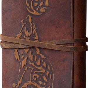 May include: A brown leather journal with a wolf and moon design. The cover features an embossed wolf howling at the moon, with a leather strap closure. The journal has a rustic, vintage aesthetic.