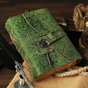 Puede incluir: Un diario de cuero verde con un dise&ntilde;o floral en relieve y un cierre en forma de llave. El diario est&aacute; cerrado y se encuentra sobre una superficie marr&oacute;n.