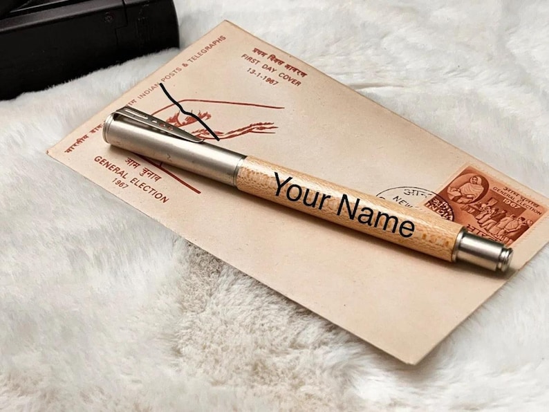 May include: A wooden pen with a silver clip and a metal tip. The pen is engraved with the text "Your Name". The pen is lying on a vintage envelope with an Indian postage stamp.