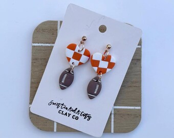 May include: Orange and white checkered heart dangle earrings with a brown football charm. The earrings are on a white card with the text "Sweet Tea and Crafty CLAY CO".