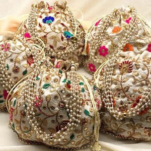 May include: Five white drawstring bags with gold embroidery and pearl embellishments. The bags have floral patterns in shades of pink, green, orange, and blue.