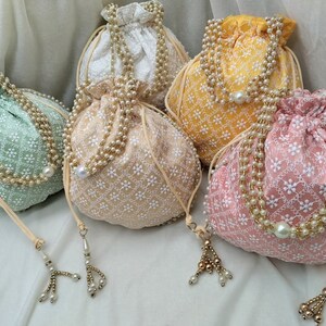 May include: Four drawstring bags with pearl embellishments and tassels. The bags are in shades of green, yellow, cream, and pink.