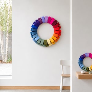 May include: A circular wall sculpture composed of numerous rectangular felt segments arranged in a vibrant rainbow gradient. The segments transition through shades of purple, pink, red, orange, yellow, green, and blue, forming a continuous ring.