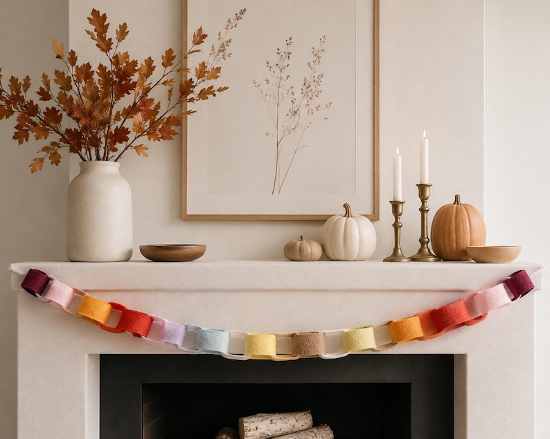 May include: A felt paper-chain style garland featuring interlocking loops in a gradient of colours including deep red, pink, orange, yellow, light blue, and tan. The garland is draped horizontally across the front of a fireplace mantel.