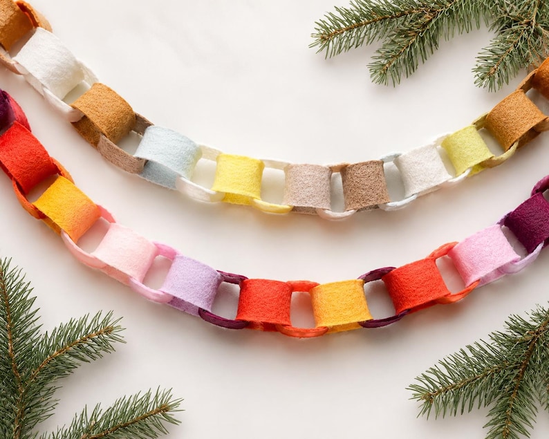May include: Two decorative garlands made of interlocking felt loops in a variety of colours including red, orange, yellow, pink, purple, white, and tan. The chains are arranged in curved lines and feature a soft, textured material finish.