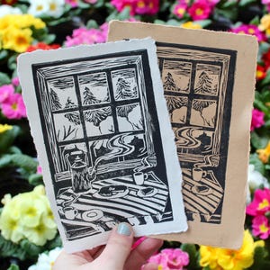 May include: Two woodblock prints of a window with a view of a forest and a table with a teapot, cups, and pastries. The prints are on a white background with a floral pattern.