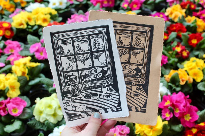May include: Two woodblock prints of a window with a view of a forest and a table with a teapot, cups, and pastries. The prints are on a white background with a floral pattern.