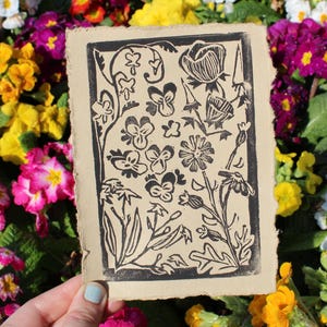 Pode incluir: Uma impress&atilde;o de lin&oacute;leo em preto e branco de um desenho floral sobre um fundo bege. A impress&atilde;o apresenta v&aacute;rias flores, folhas e caules.