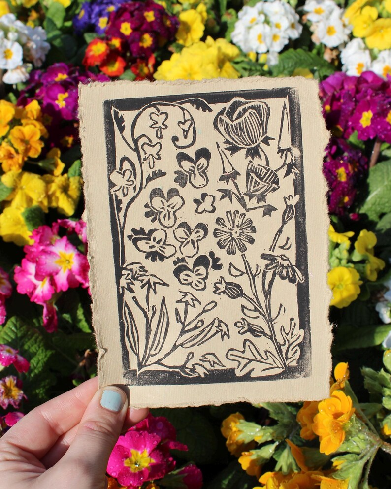 Pode incluir: Uma impress&atilde;o de lin&oacute;leo em preto e branco de um desenho floral sobre um fundo bege. A impress&atilde;o apresenta v&aacute;rias flores, folhas e caules.
