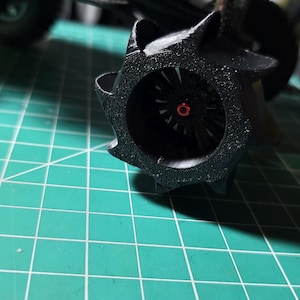 Puede incluir: Primer plano de una rueda de camión de plástico negro con un cubo central rojo. La rueda está sobre una estera de corte verde.