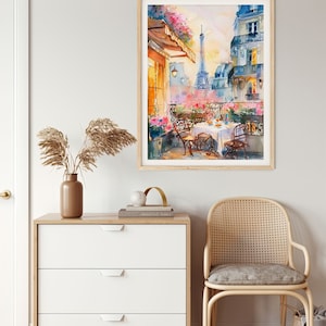 May include: Watercolor painting of a Parisian balcony with a view of the Eiffel Tower. The balcony has a table set for a meal with two chairs. The painting is framed in a light wood frame.