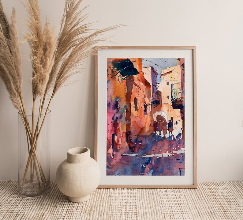 May include: Watercolor painting of a sunlit street scene in a wooden frame. The artwork features buildings in shades of orange, pink, and blue, with silhouetted figures. The painting evokes a warm, Mediterranean atmosphere.