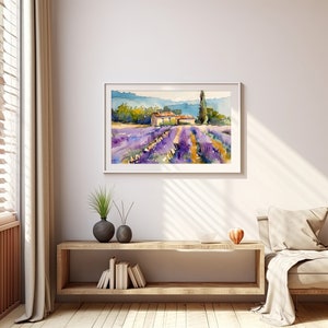 K&ouml;nnte beinhalten: Ein Aquarellbild eines Lavendelfeldes mit einem kleinen Haus und einem hohen Baum im Hintergrund. Das Bild ist in einem wei&szlig;en Rahmen gerahmt und h&auml;ngt an einer wei&szlig;en Wand.
