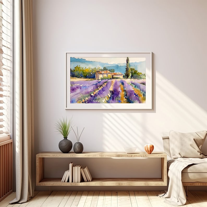 K&ouml;nnte beinhalten: Ein Aquarellbild eines Lavendelfeldes mit einem kleinen Haus und einem hohen Baum im Hintergrund. Das Bild ist in einem wei&szlig;en Rahmen gerahmt und h&auml;ngt an einer wei&szlig;en Wand.