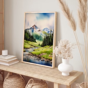 May include: A framed watercolour painting of a mountain landscape with a river flowing through a valley. The painting is in a light wood frame and is hanging on a wall above a wooden bench.