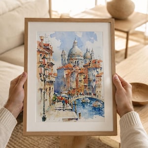 May include: A framed watercolor painting depicting a Venetian canal scene with the Santa Maria della Salute basilica in the background. The artwork features warm orange and red buildings, a blue waterway with boats, and a tall black street lamp.