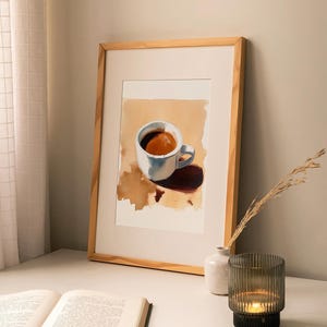 Puede incluir: Una pintura de acuarela enmarcada de una taza de caf&eacute; blanca con un l&iacute;quido marr&oacute;n en su interior. La taza est&aacute; sobre una superficie marr&oacute;n con una mancha marr&oacute;n. La pintura est&aacute; en un marco de madera.
