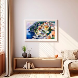 May include: A watercolour painting of a colourful Italian village built on a hillside overlooking the sea. The buildings are painted in shades of yellow, orange, pink, and blue. The sea is a deep blue, and the sky is a light blue.