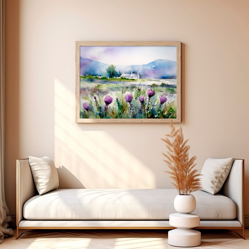 May include: A watercolor painting of a white cottage in a field of purple wildflowers, framed in a light wood frame and hanging on a beige wall above a white couch.