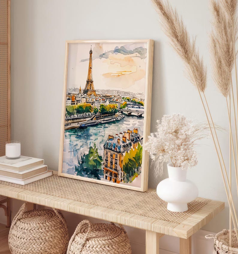 Puede incluir: Una pintura de acuarela de la Torre Eiffel en Par&iacute;s, Francia. La pintura muestra la torre en la distancia con un r&iacute;o y edificios en primer plano. La pintura est&aacute; enmarcada en un marco de madera claro y est&aacute; colgada en una pared.