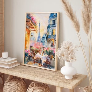 May include: A watercolor painting of a Parisian balcony scene with a view of the Eiffel Tower. The balcony is decorated with flowers and there is a table set for a meal with two chairs. The painting is framed in a light wood frame.
