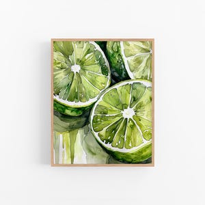 Puede incluir: Pintura de acuarela enmarcada de limas en rodajas. Las limas son de un verde vibrante con centros blancos, mostrando sus jugosos interiores. La obra de arte tiene un ambiente fresco y veraniego, perfecto para la decoración de la cocina o el comedor.