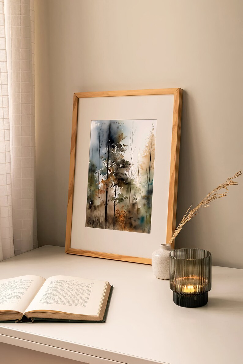 May include: A framed watercolor painting of a forest scene with trees in shades of brown, green, and blue. The painting is on a white table with a book and a candle holder.