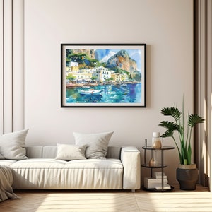 May include: Watercolour painting of a coastal town with colourful buildings and a boat in the water. The painting is framed in black and hanging on a white wall.