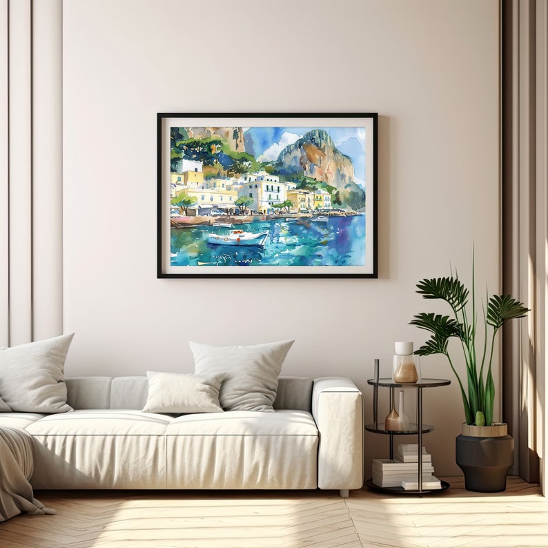 May include: Watercolour painting of a coastal town with colourful buildings and a boat in the water. The painting is framed in black and hanging on a white wall.