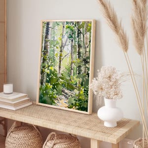 May include: A watercolor painting of a forest scene with tall trees and green foliage. The painting is framed in a light wood frame and is hanging on a wall.