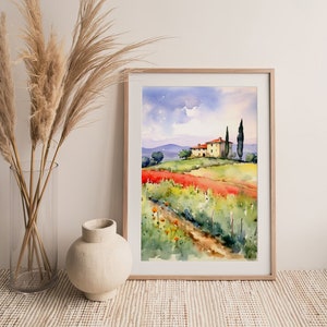 May include: A watercolor painting of a yellow house with a red tile roof on a hill overlooking a field of red flowers. Two tall green trees stand beside the house. The painting is framed in a light wood frame.