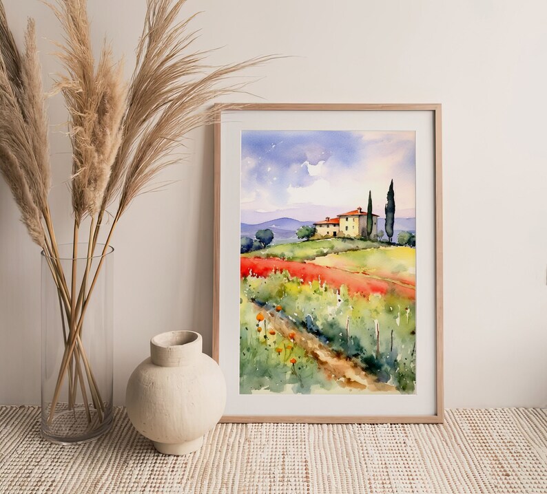 May include: A watercolor painting of a yellow house with a red tile roof on a hill overlooking a field of red flowers. Two tall green trees stand beside the house. The painting is framed in a light wood frame.