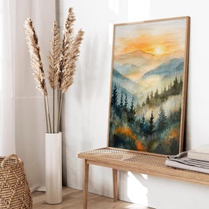 May include: A framed watercolor painting depicts a mountain landscape with a sunset. The artwork features layers of blue and green mountains, with a bright orange and yellow sky. The painting is displayed on a wooden bench.